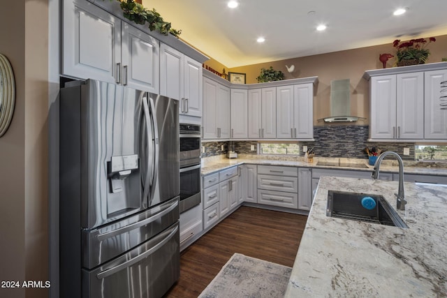 kitchen with light stone countertops, sink, wall chimney range hood, and appliances with stainless steel finishes