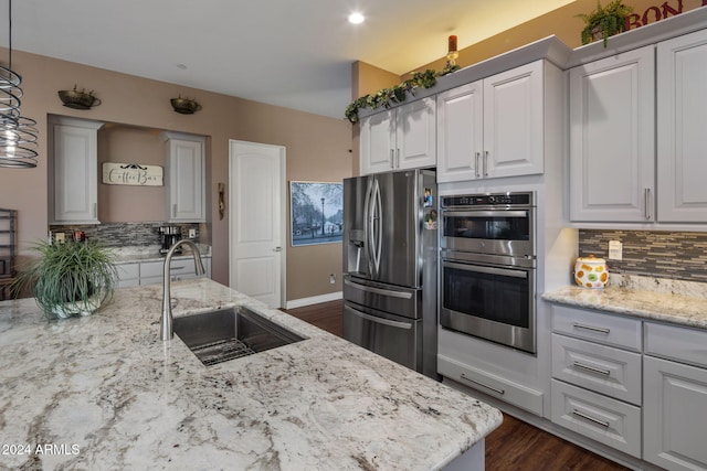 kitchen with white cabinetry, sink, hanging light fixtures, stainless steel appliances, and decorative backsplash