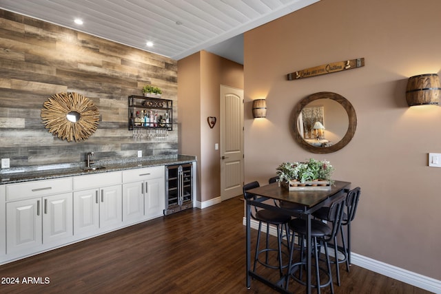 bar with wood walls, dark stone countertops, white cabinetry, and wine cooler