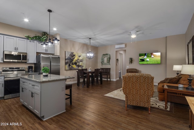 kitchen with light stone counters, stainless steel appliances, ceiling fan, decorative light fixtures, and a center island