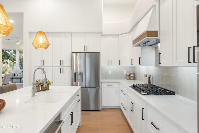 kitchen with custom exhaust hood, white cabinets, sink, light stone countertops, and stainless steel appliances