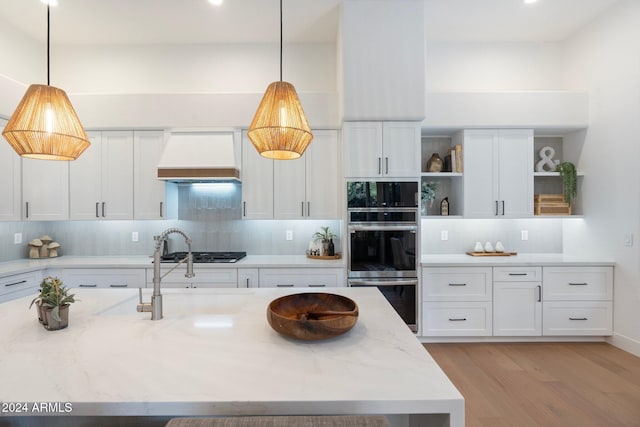 kitchen featuring white cabinetry, stainless steel appliances, light stone counters, decorative light fixtures, and custom range hood