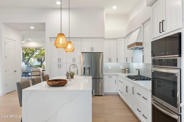 kitchen featuring white cabinets, custom range hood, stainless steel appliances, and hanging light fixtures