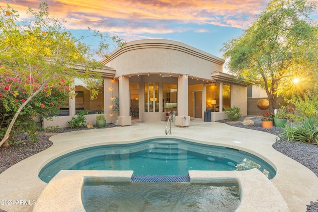 back house at dusk featuring a swimming pool with hot tub and a patio