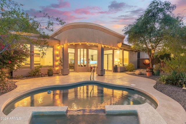 pool at dusk with an in ground hot tub and a patio