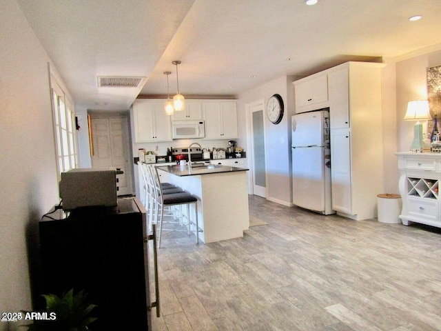 kitchen with a breakfast bar area, white cabinetry, hanging light fixtures, light hardwood / wood-style flooring, and white appliances