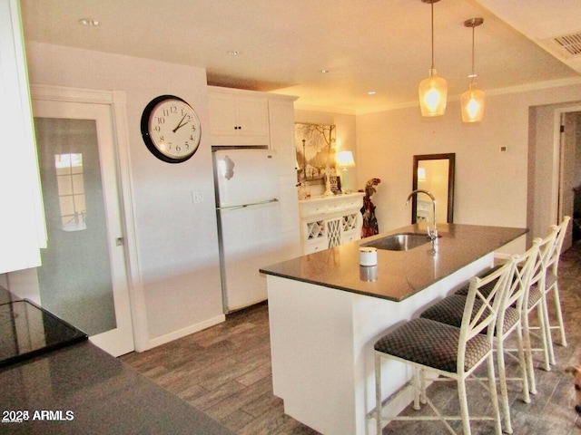 kitchen featuring a breakfast bar, sink, white refrigerator, pendant lighting, and white cabinets