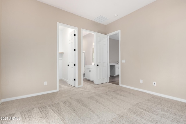 unfurnished bedroom featuring a spacious closet, light carpet, ensuite bathroom, and a closet