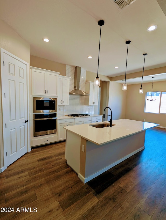 kitchen with wall chimney range hood, sink, decorative light fixtures, white cabinets, and dark hardwood / wood-style flooring