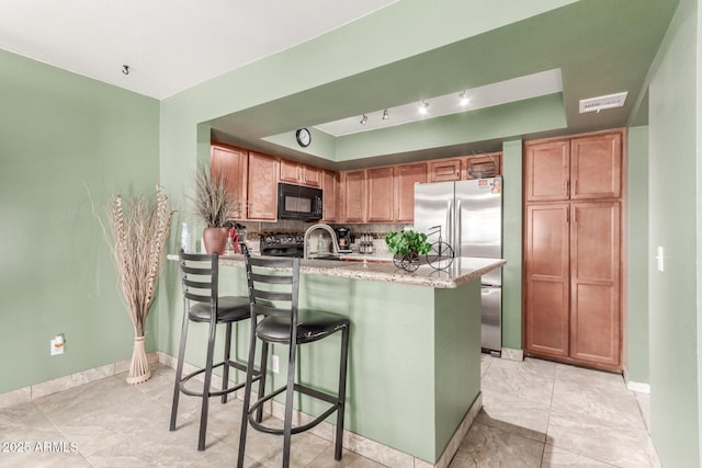 kitchen featuring light stone countertops, a breakfast bar, black appliances, backsplash, and sink