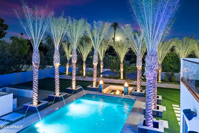 pool at dusk featuring pool water feature and a lawn