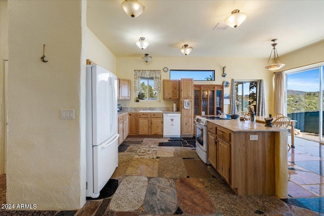 kitchen with white appliances, light countertops, stone finish flooring, a sink, and pendant lighting