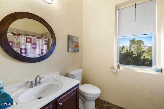 bathroom with toilet, curtained shower, a textured wall, and vanity