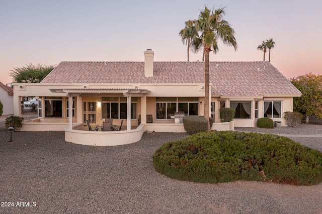 back house at dusk featuring a pergola and a patio