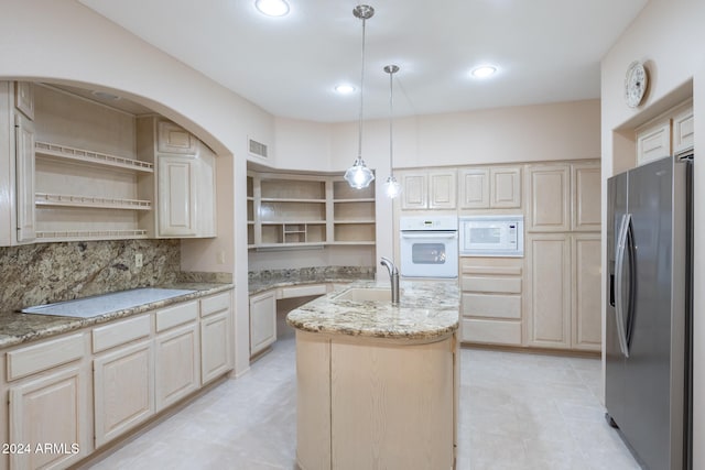 kitchen with light stone countertops, a center island with sink, white appliances, and sink