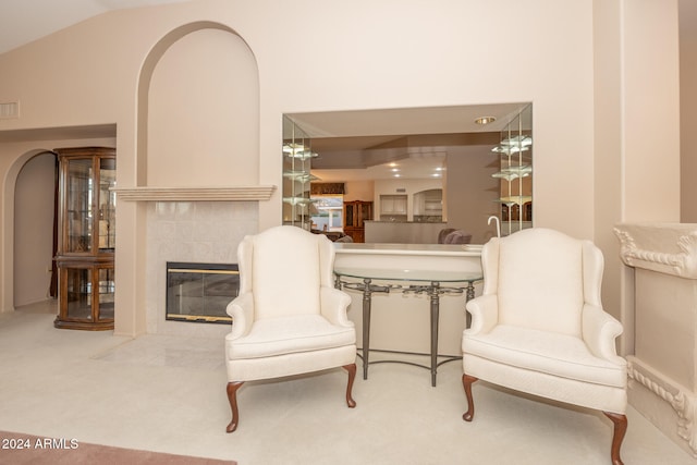 living area with high vaulted ceiling, light colored carpet, and a tile fireplace