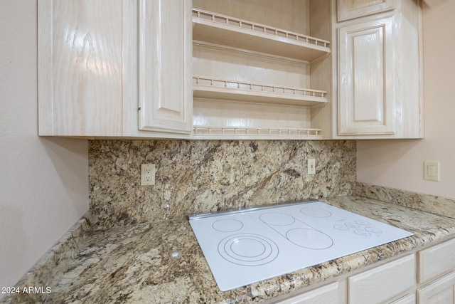 interior details featuring backsplash, white electric stovetop, and light stone counters