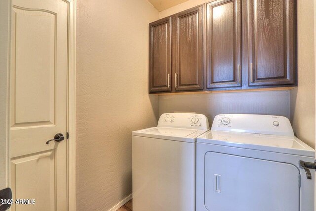 laundry room featuring washing machine and dryer, cabinet space, and a textured wall