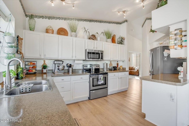 kitchen featuring appliances with stainless steel finishes, decorative backsplash, a towering ceiling, white cabinets, and sink