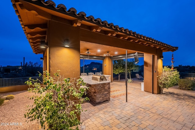 patio at twilight with area for grilling, fence, and a ceiling fan