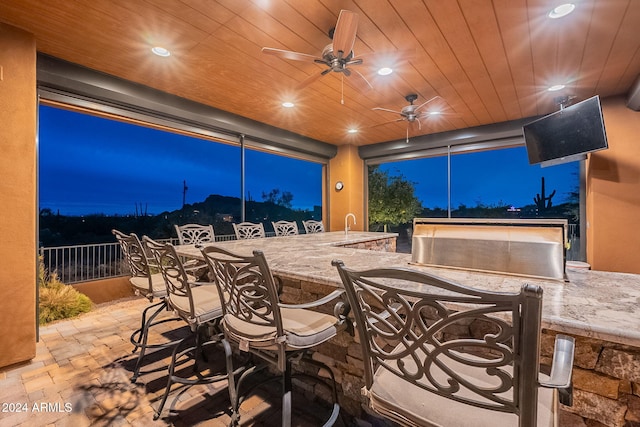 view of patio with exterior bar, ceiling fan, fence, and outdoor dining space