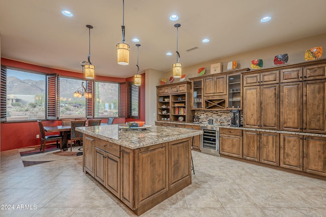 kitchen featuring light stone counters, wine cooler, pendant lighting, a center island, and glass insert cabinets