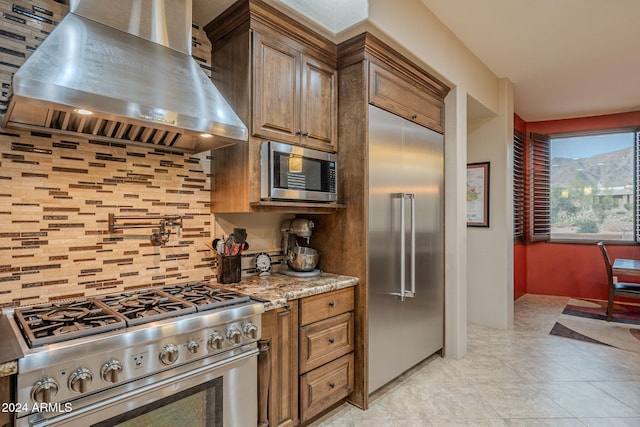 kitchen with light tile patterned floors, decorative backsplash, light stone countertops, stainless steel appliances, and extractor fan