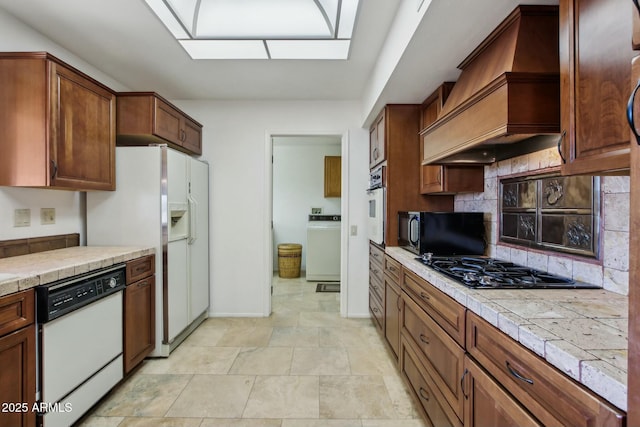 kitchen featuring backsplash, black appliances, tile countertops, washer / dryer, and custom exhaust hood