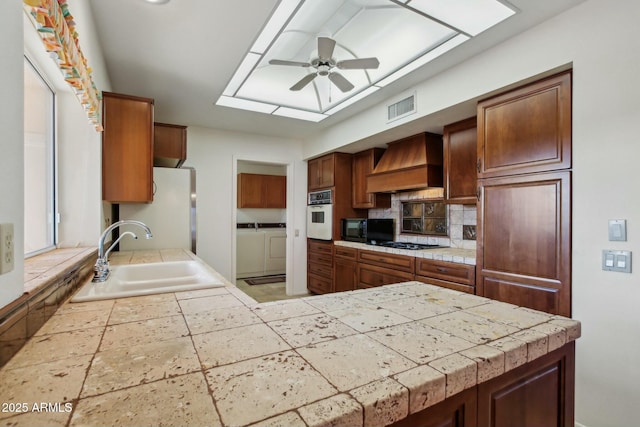 kitchen featuring tile countertops, sink, custom exhaust hood, black appliances, and washer and clothes dryer