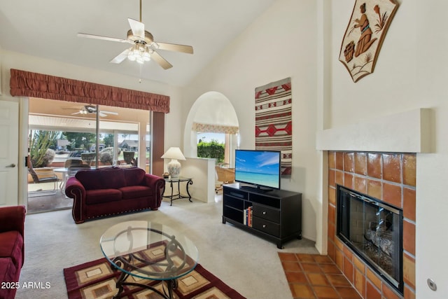 carpeted living room featuring high vaulted ceiling, a tile fireplace, and ceiling fan