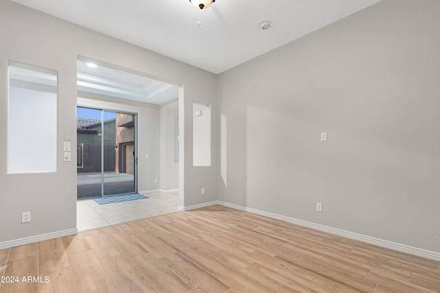 unfurnished room with light wood-type flooring, a raised ceiling, and a wealth of natural light