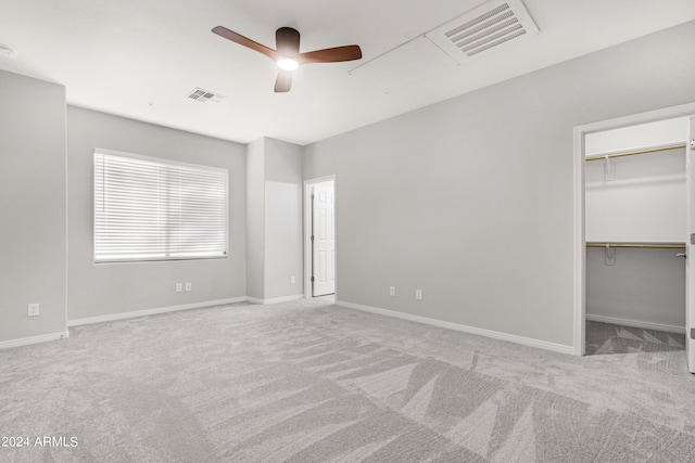 unfurnished bedroom featuring light carpet, a walk in closet, and ceiling fan