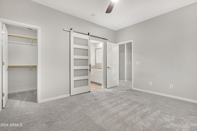 unfurnished bedroom with a barn door, ceiling fan, a closet, a walk in closet, and light colored carpet