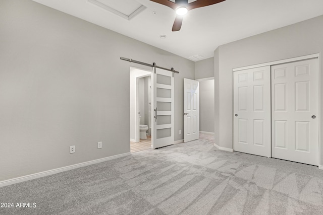 unfurnished bedroom featuring light colored carpet, ceiling fan, a barn door, and a closet