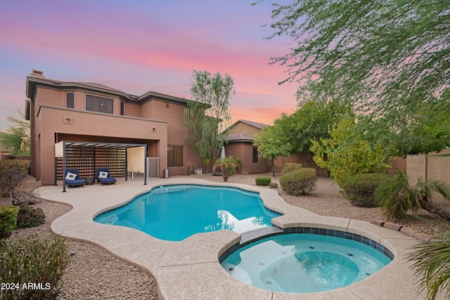 pool at dusk with an in ground hot tub and a patio area