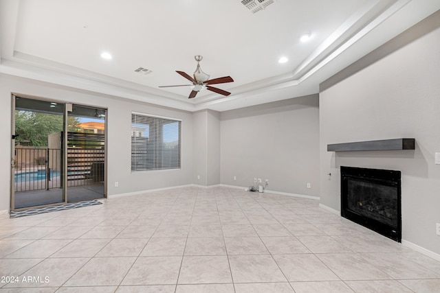 unfurnished living room featuring a tray ceiling, light tile patterned flooring, and ceiling fan