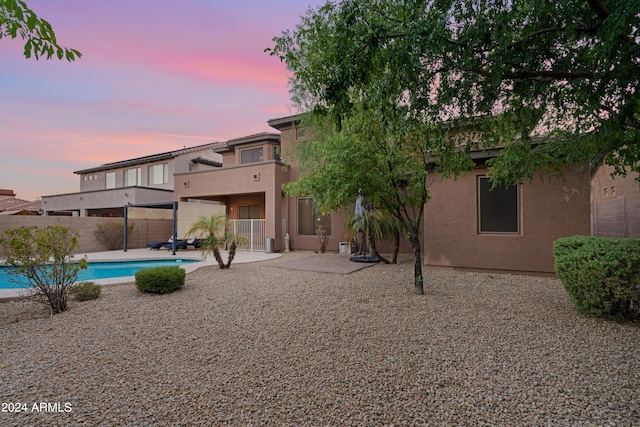 back house at dusk featuring a fenced in pool and a patio area