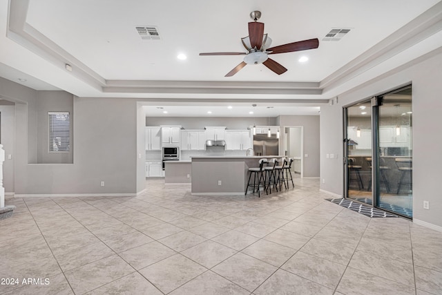 unfurnished living room with ceiling fan, sink, light tile patterned floors, and a tray ceiling