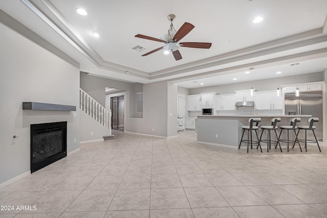 living room featuring ceiling fan, a tray ceiling, and light tile patterned flooring