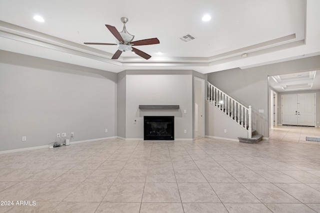 unfurnished living room with a tray ceiling, light tile patterned floors, and ceiling fan