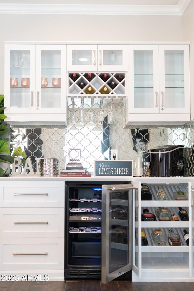 bar with wine cooler, decorative backsplash, white cabinetry, and ornamental molding