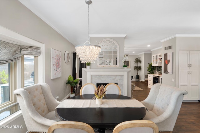 dining area featuring a fireplace, dark hardwood / wood-style flooring, crown molding, and a chandelier