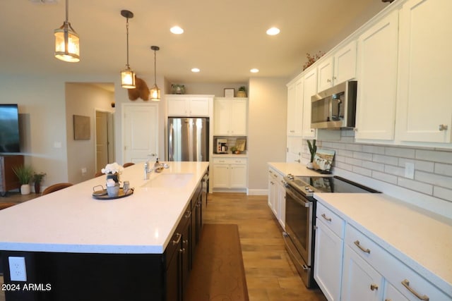 kitchen featuring backsplash, a kitchen island with sink, hanging light fixtures, white cabinetry, and stainless steel appliances