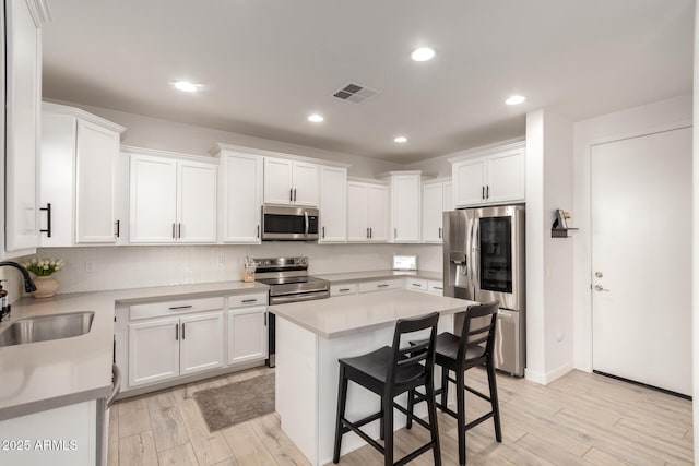 kitchen featuring sink, appliances with stainless steel finishes, a kitchen breakfast bar, white cabinets, and a kitchen island