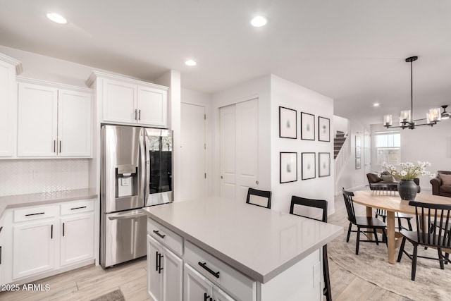 kitchen with stainless steel refrigerator with ice dispenser, decorative light fixtures, a kitchen breakfast bar, a kitchen island, and white cabinets