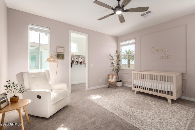 bedroom featuring a walk in closet, a nursery area, ceiling fan, and carpet