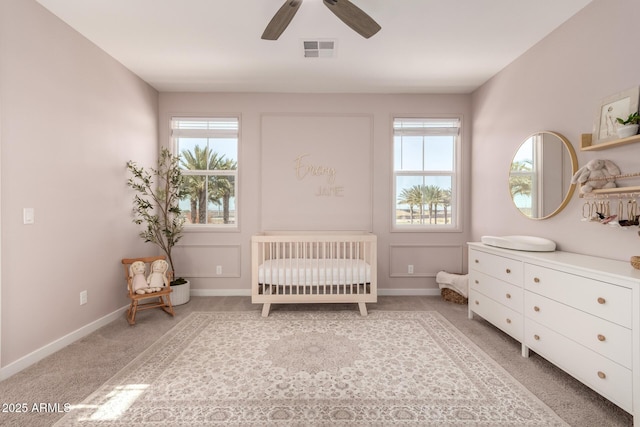 carpeted bedroom featuring a nursery area, ceiling fan, and multiple windows