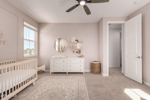 carpeted bedroom with a crib and ceiling fan