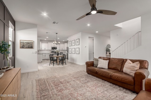 living room featuring ceiling fan with notable chandelier and light hardwood / wood-style flooring