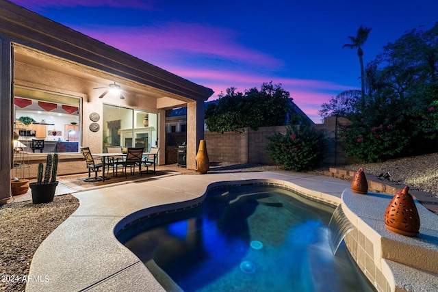 pool at dusk with ceiling fan and a patio